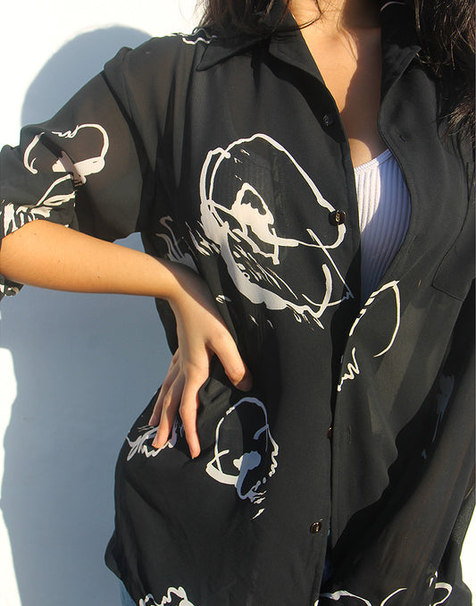 Woman wearing a black shirt with white floral print against a white wall.