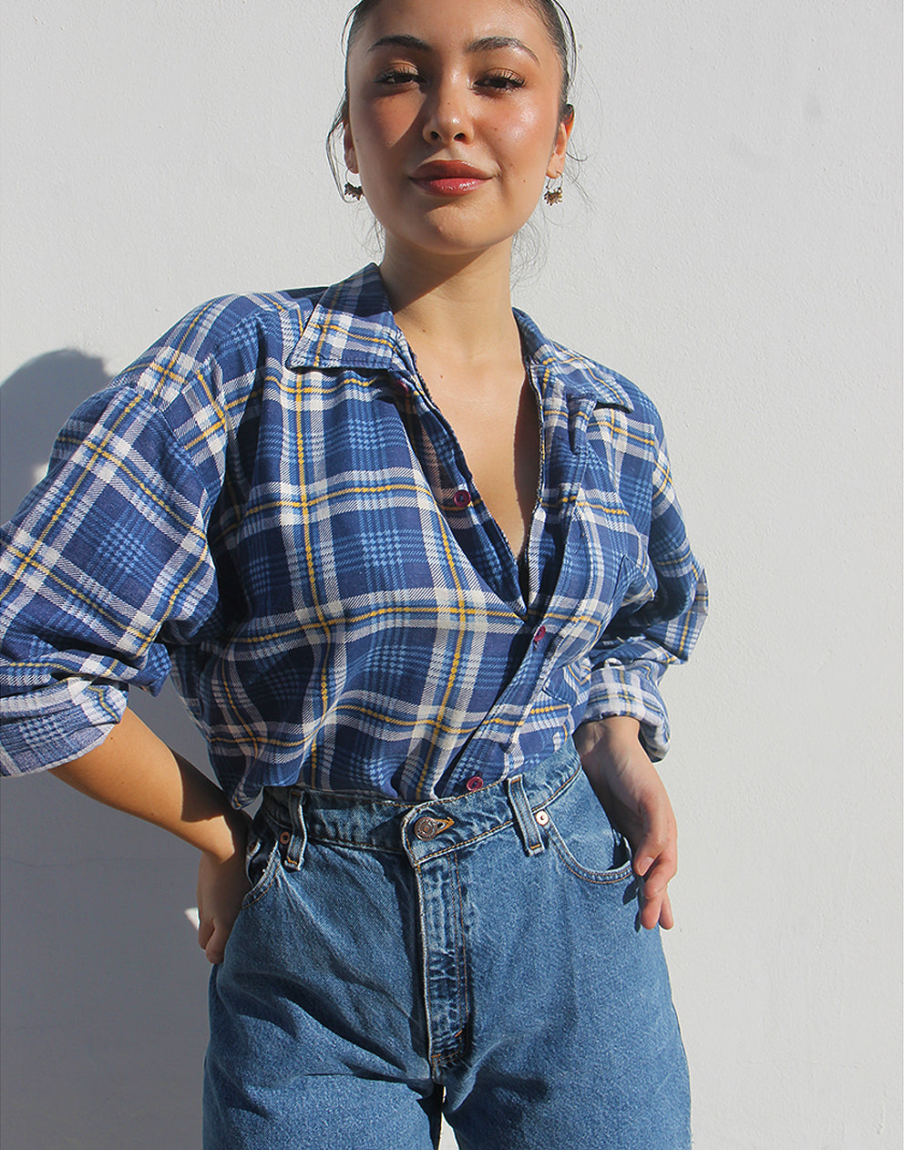 Person wearing a blue plaid shirt and jeans against a plain background