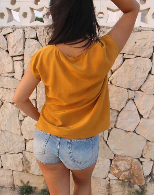Person wearing a yellow top and denim shorts against a stone wall.