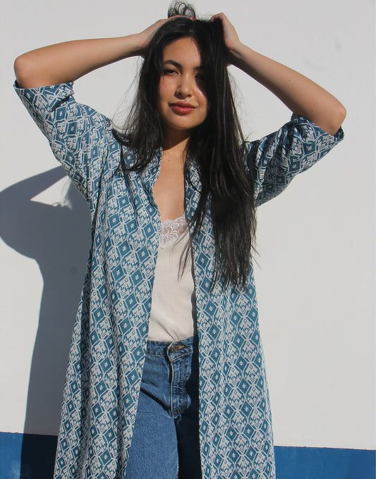 WOMAN WEARING A LONG BLUE JACKET AGAINST A WHITE WALL