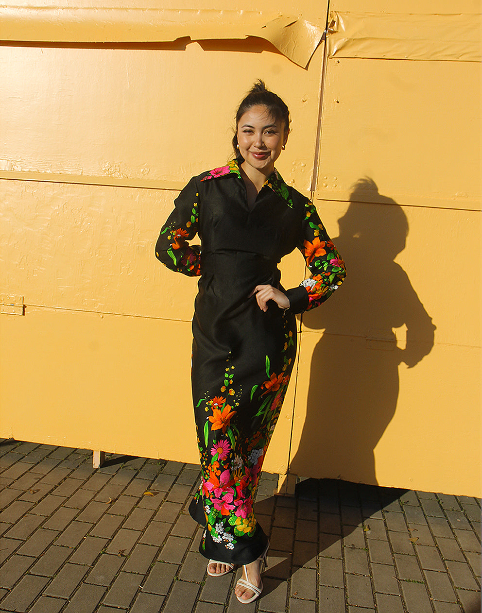 WOMAN WEARING 70S BLACK VINTAGE DRESS WITH FLORAL PRINT AGAINST A YELLOW WALL