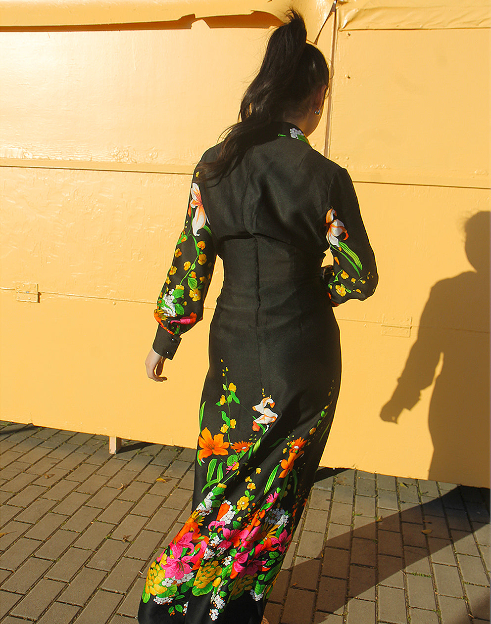 WOMAN WEARING 70S BLACK VINTAGE DRESS WITH FLORAL PRINT AGAINST A YELLOW WALL