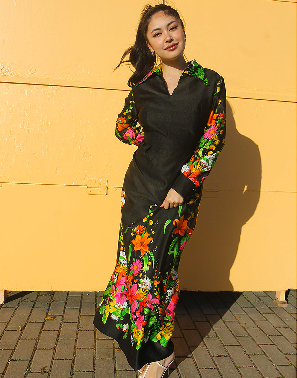 WOMAN WEARING 70S BLACK VINTAGE DRESS WITH FLORAL PRINT AGAINST A YELLOW WALL