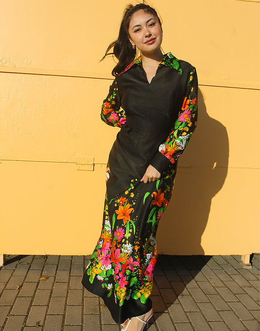 WOMAN WEARING 70S BLACK VINTAGE DRESS WITH FLORAL PRINT AGAINST A YELLOW WALL