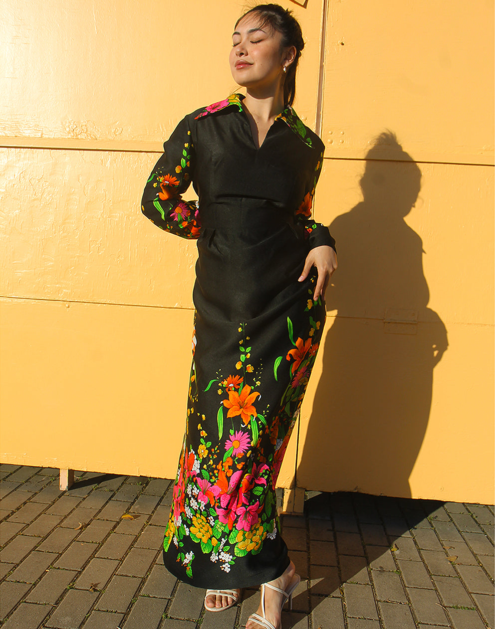 WOMAN WEARING 70S BLACK VINTAGE DRESS WITH FLORAL PRINT AGAINST A YELLOW WALL
