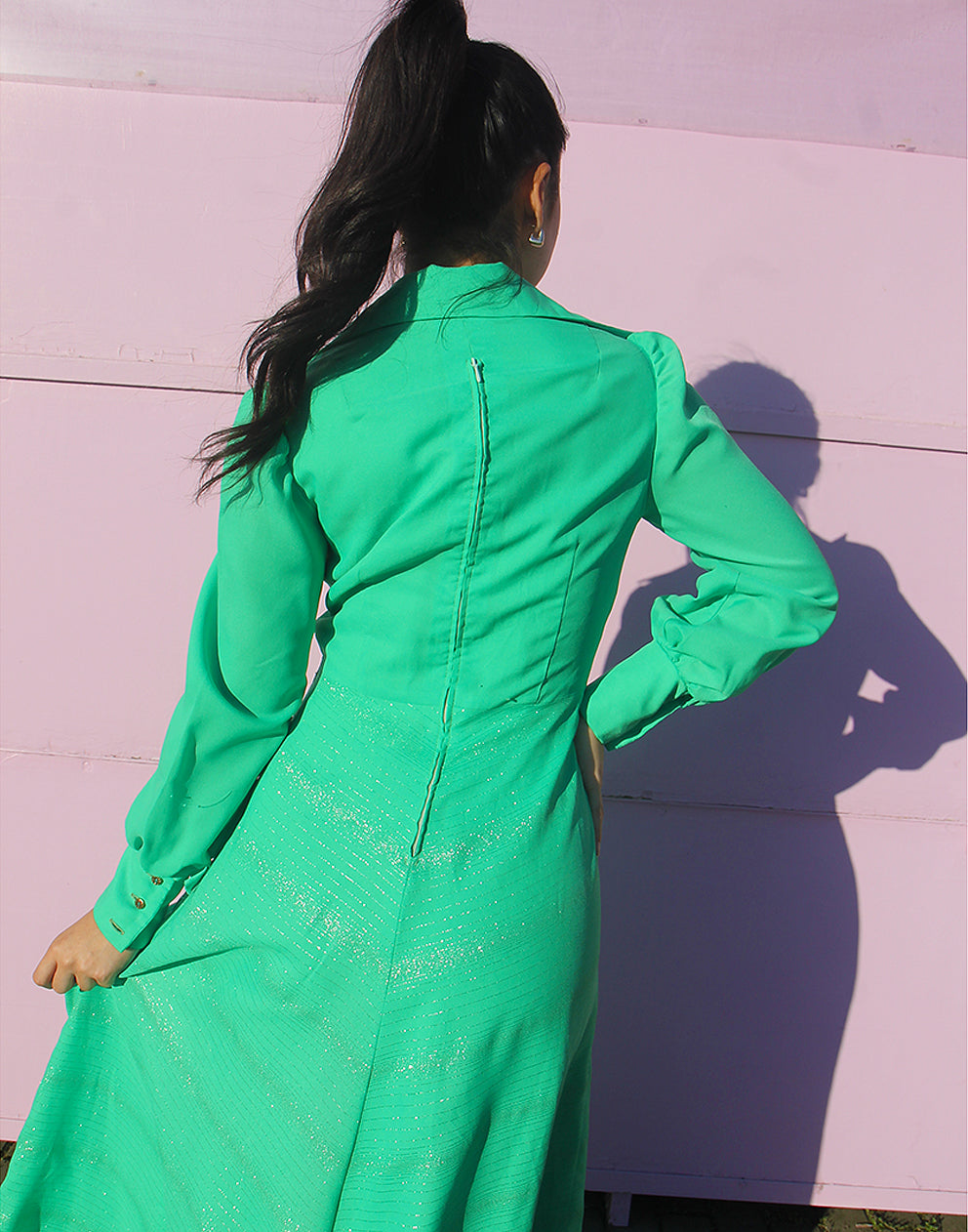 woman in green 70s long sleeve maxi dress against a pink wall 