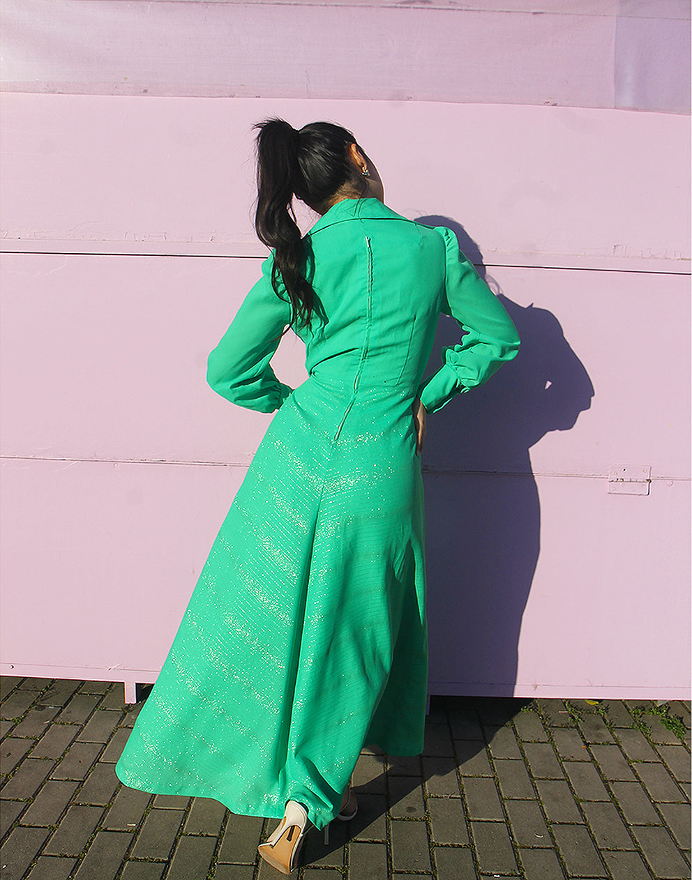 woman in green 70s long sleeve maxi dress against a pink wall 