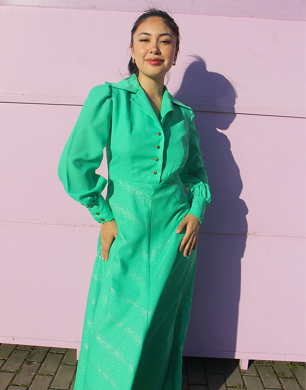 woman in green 70s long sleeve maxi dress against a pink wall 