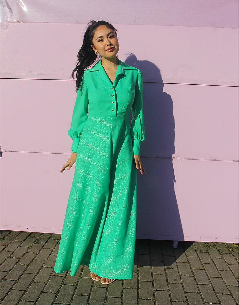 woman in green 70s long sleeve maxi dress against a pink wall 