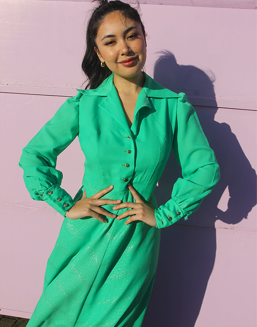 woman in green 70s long sleeve maxi dress against a pink wall 