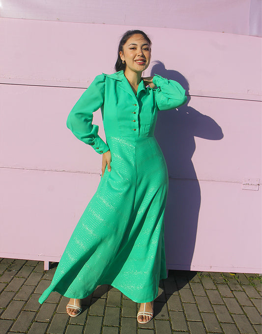 woman in green 70s long sleeve maxi dress against a pink wall 