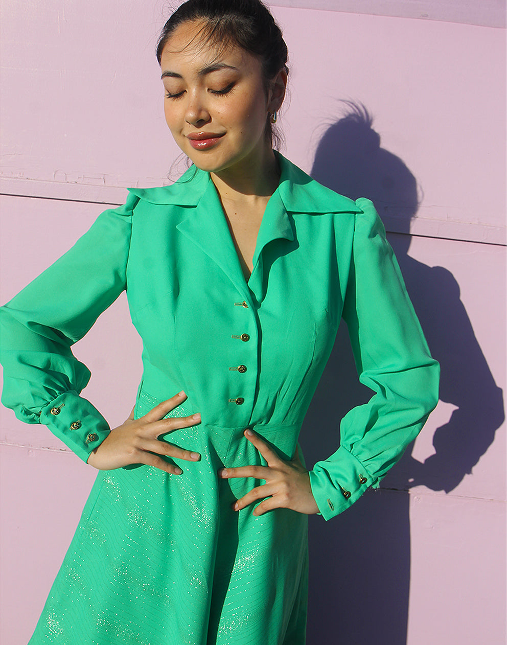 woman in green 70s long sleeve maxi dress against a pink wall 