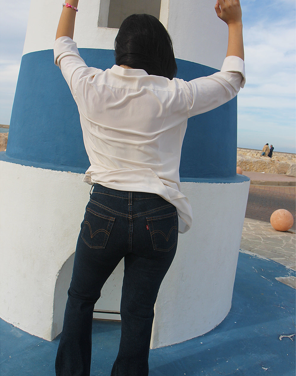 Woman wearing long sleeve Beige Silk Shirt against a blue and white wall