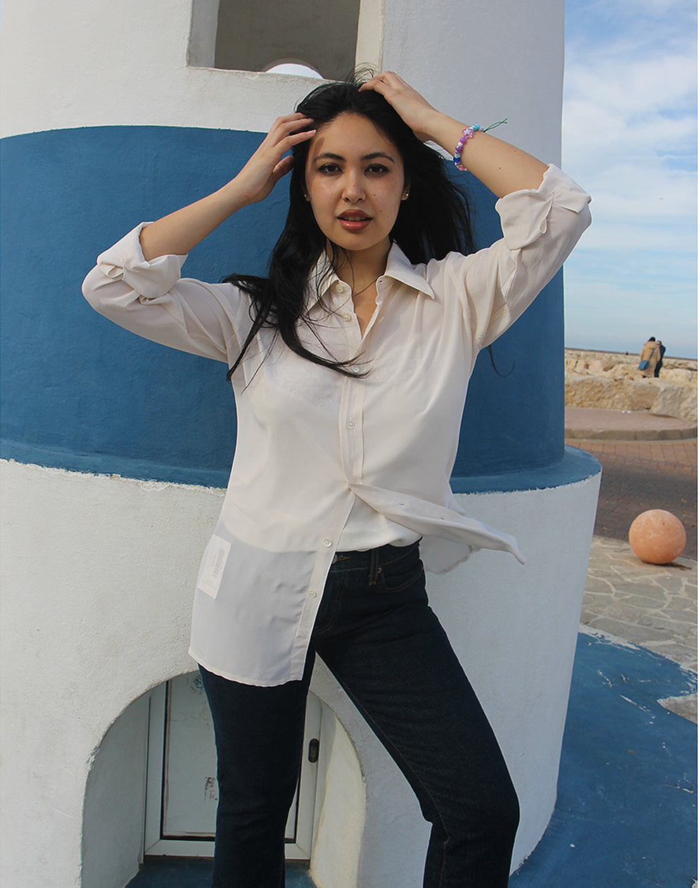 Woman wearing long sleeve Beige Silk Shirt against a blue and white wall