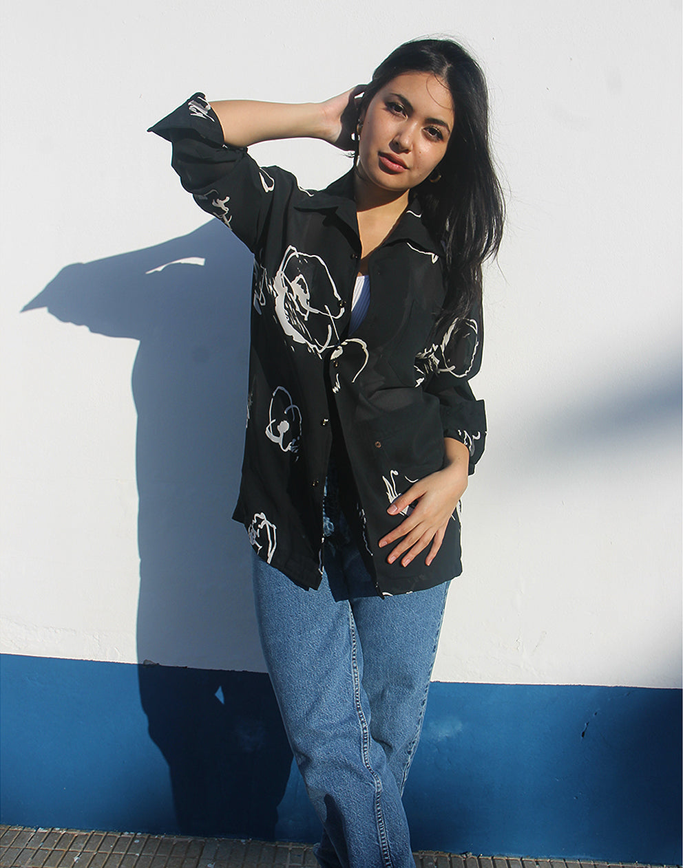 Woman wearing a black shirt with white floral print against a white wall.