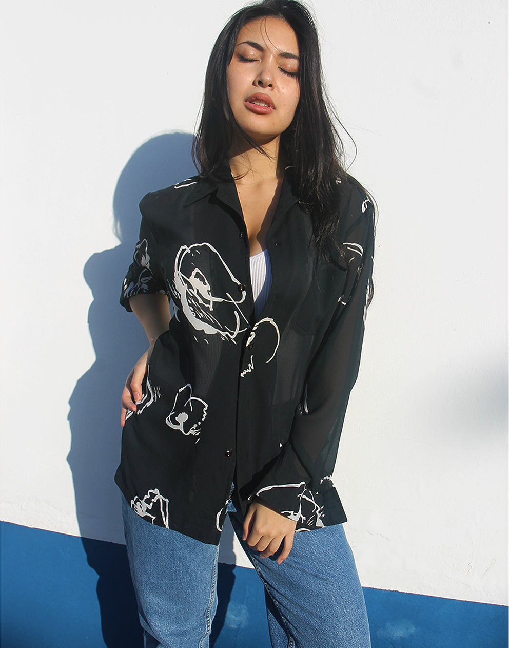 Woman wearing a black shirt with white floral print against a white wall.