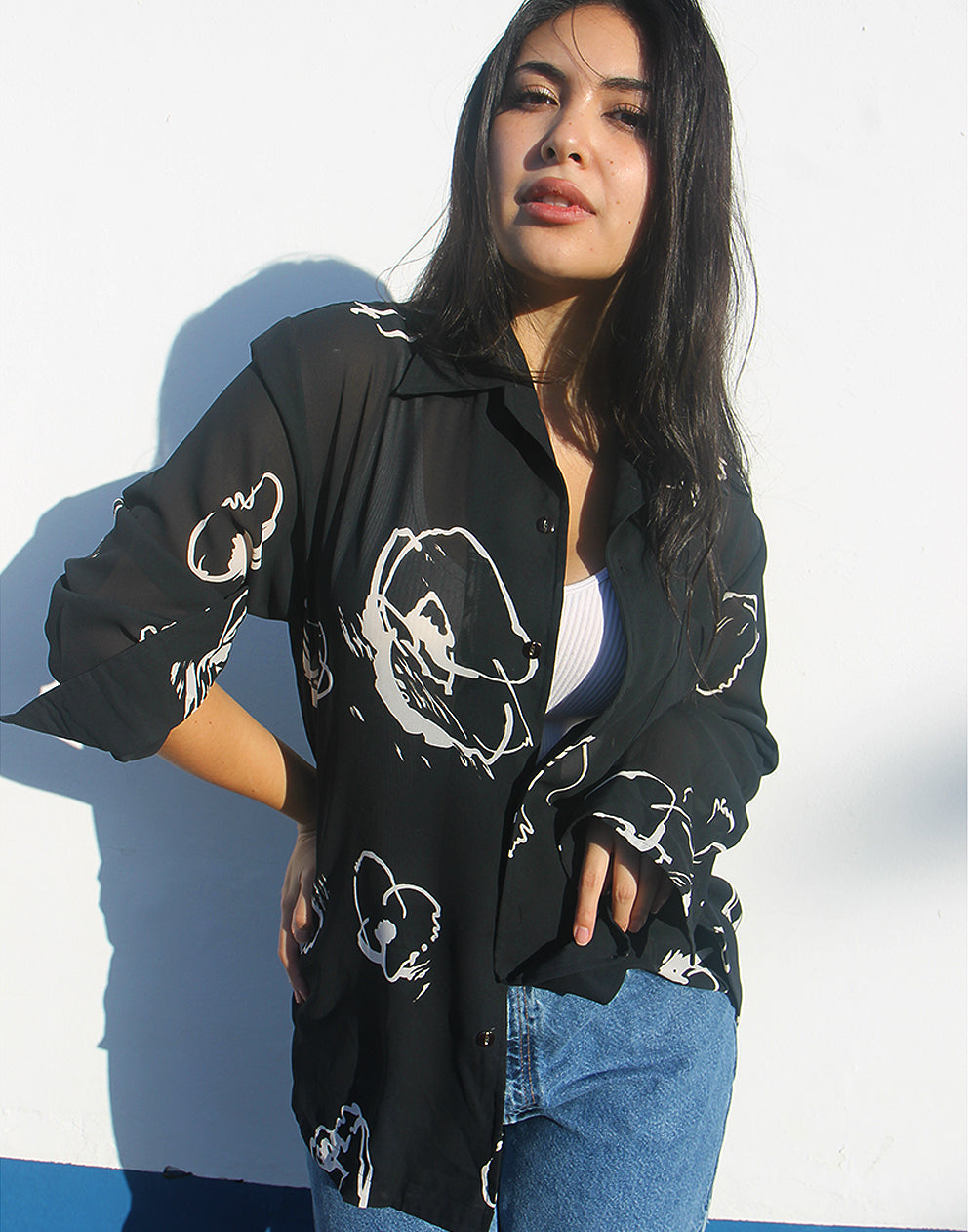 Woman wearing a black shirt with white floral print against a white wall.