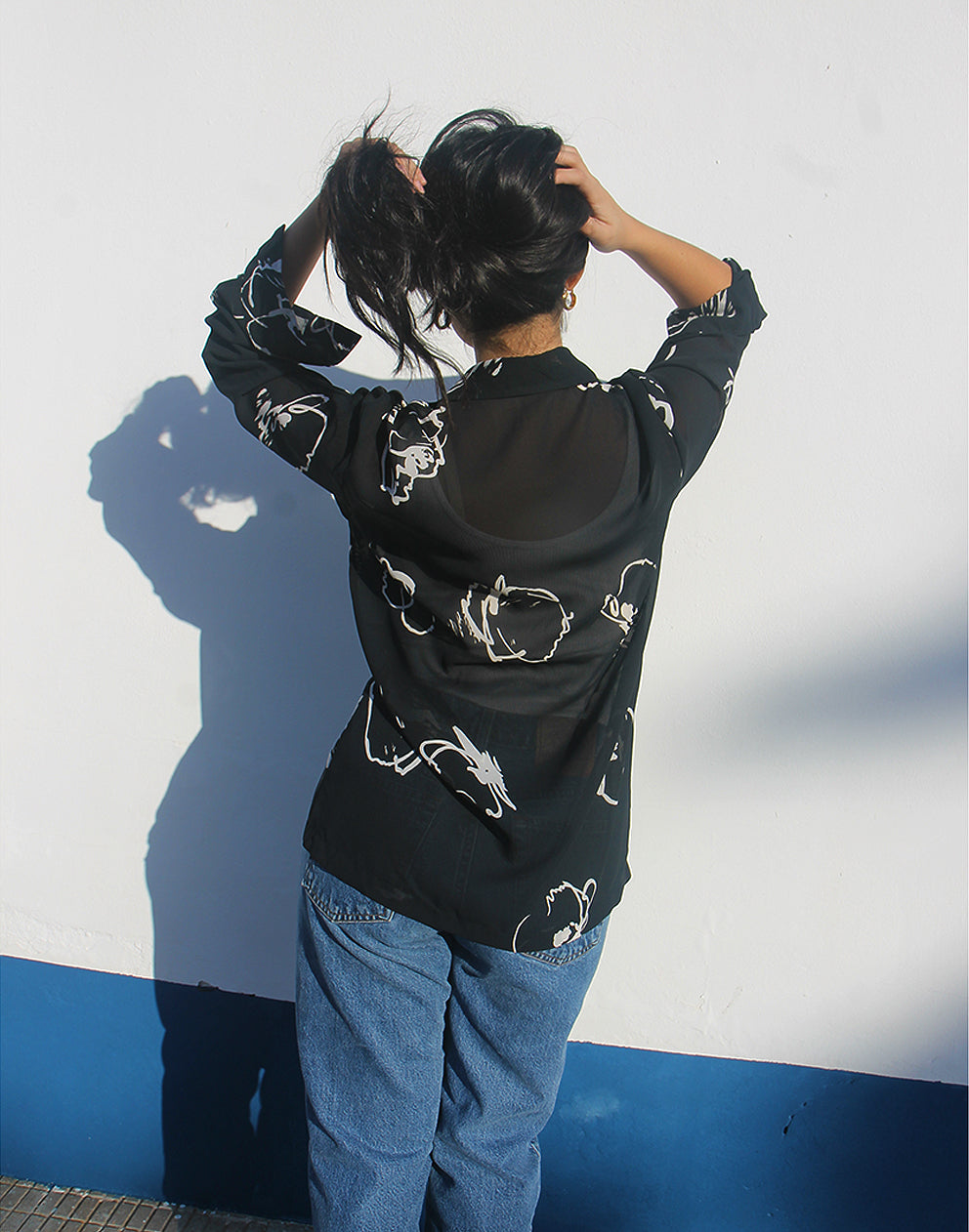 Woman wearing a black shirt with white floral print against a white wall.