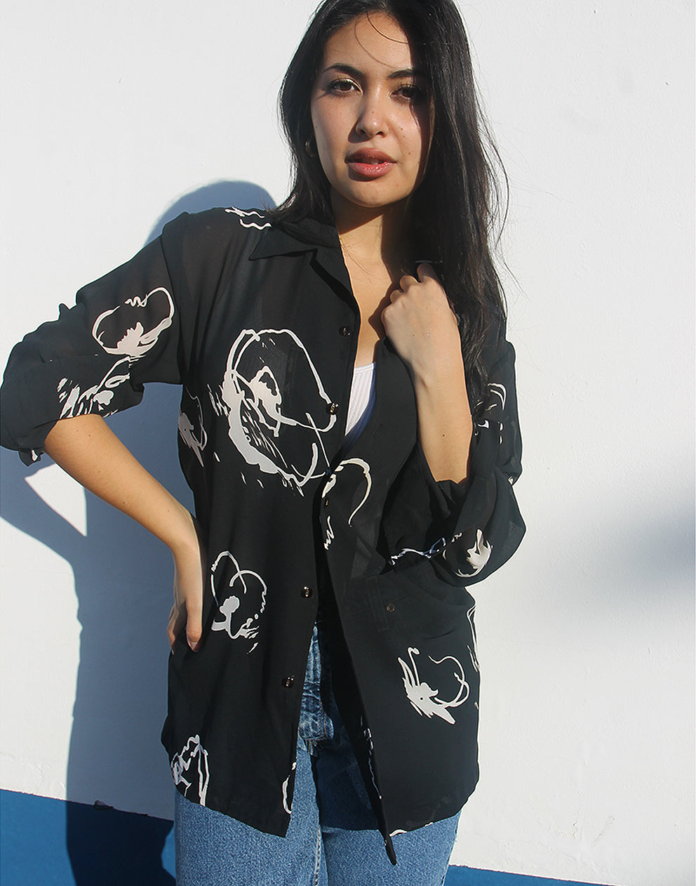 Woman wearing a black shirt with white floral print against a white wall.