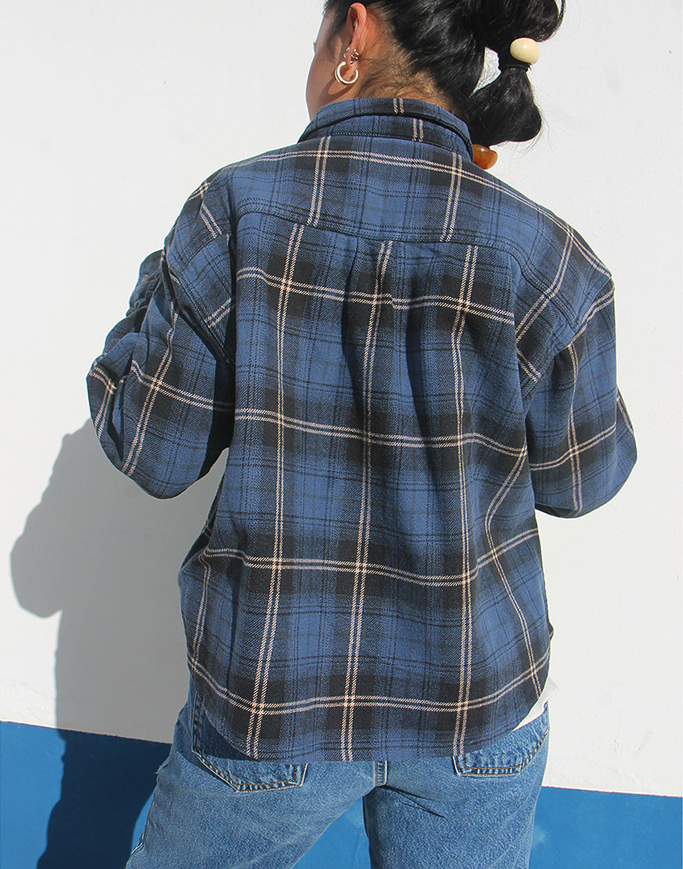 Person wearing a blue plaid shirt and jeans against a white background