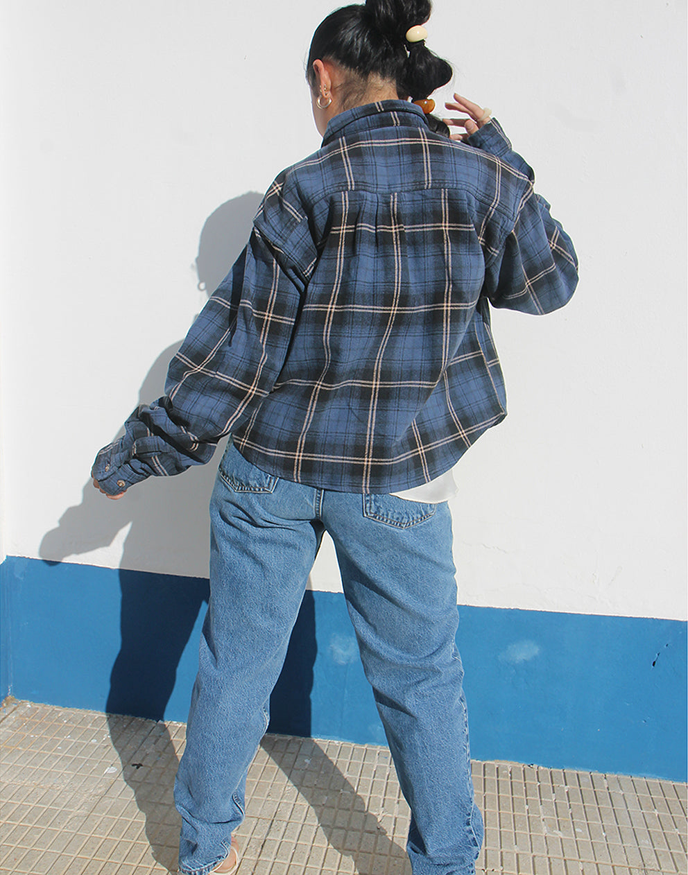 Person wearing a blue plaid shirt and jeans against a white background