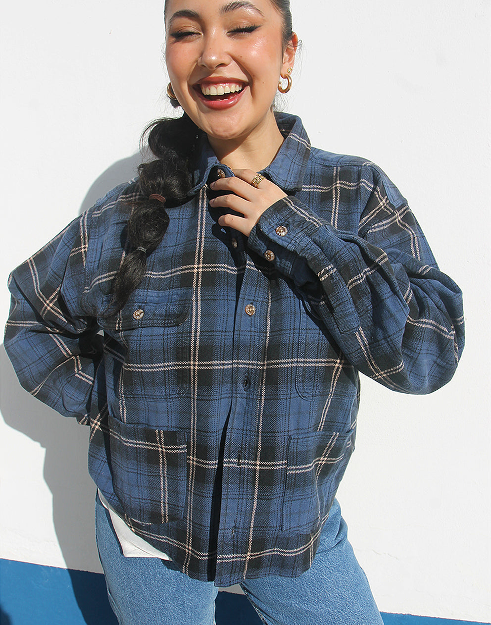 Person wearing a blue plaid shirt and jeans against a white background