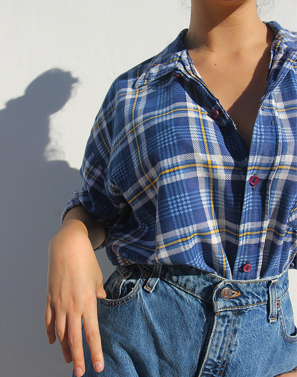 Person wearing a blue plaid shirt and jeans against a light background