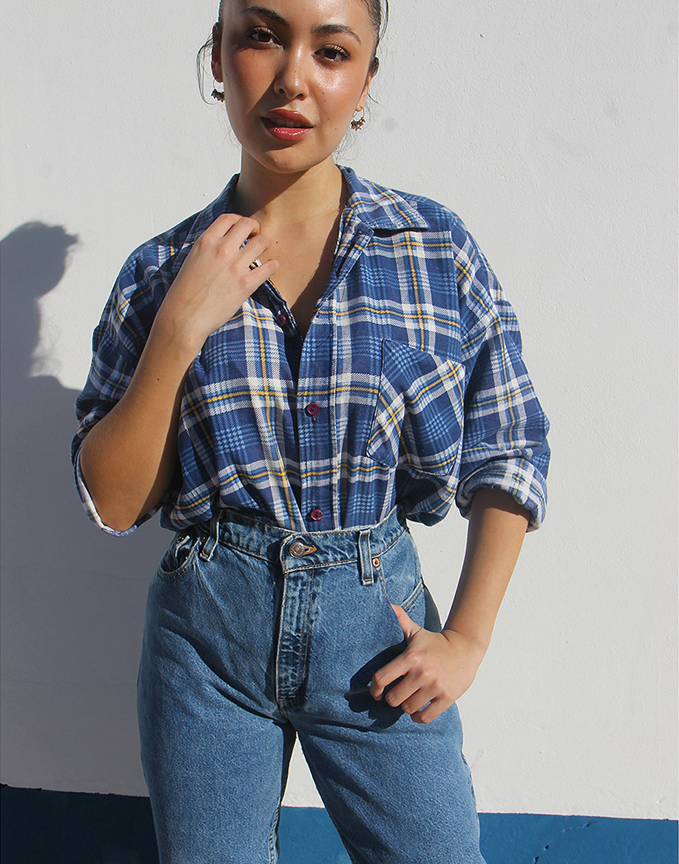 Person wearing a blue plaid shirt and jeans against a plain background