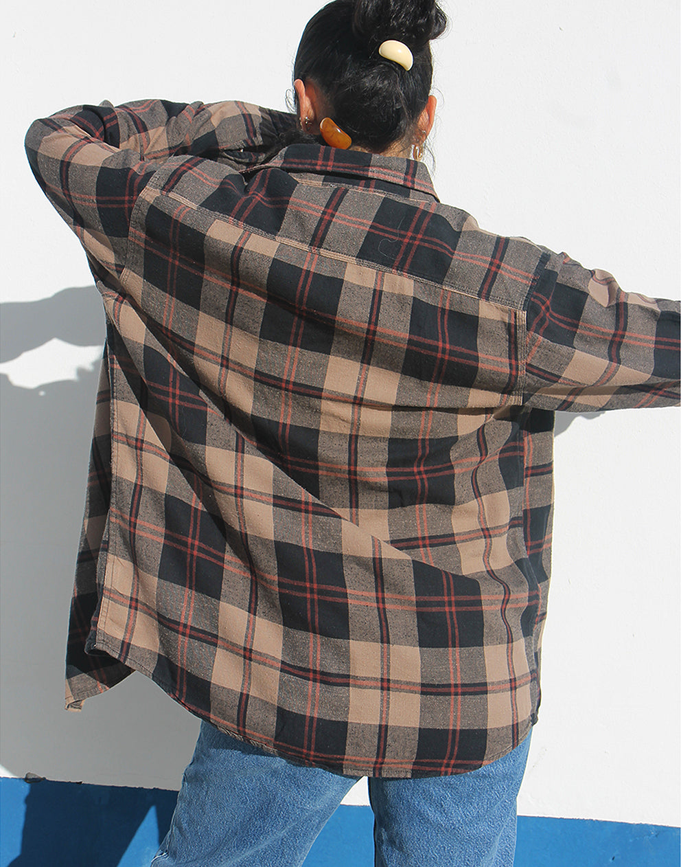 Woman wearing a brown plaid shirt and jeans against a white background