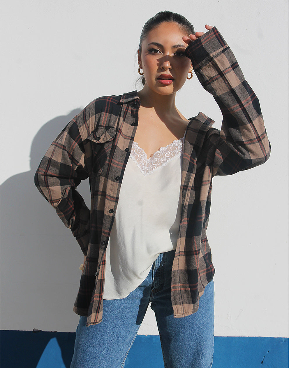 Woman wearing a brown plaid shirt and womens vintage jeans against a white background