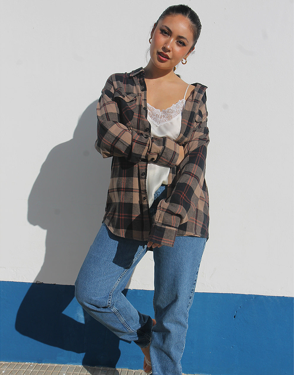 Woman wearing a brown plaid shirt and womens vintage jeans against a white background