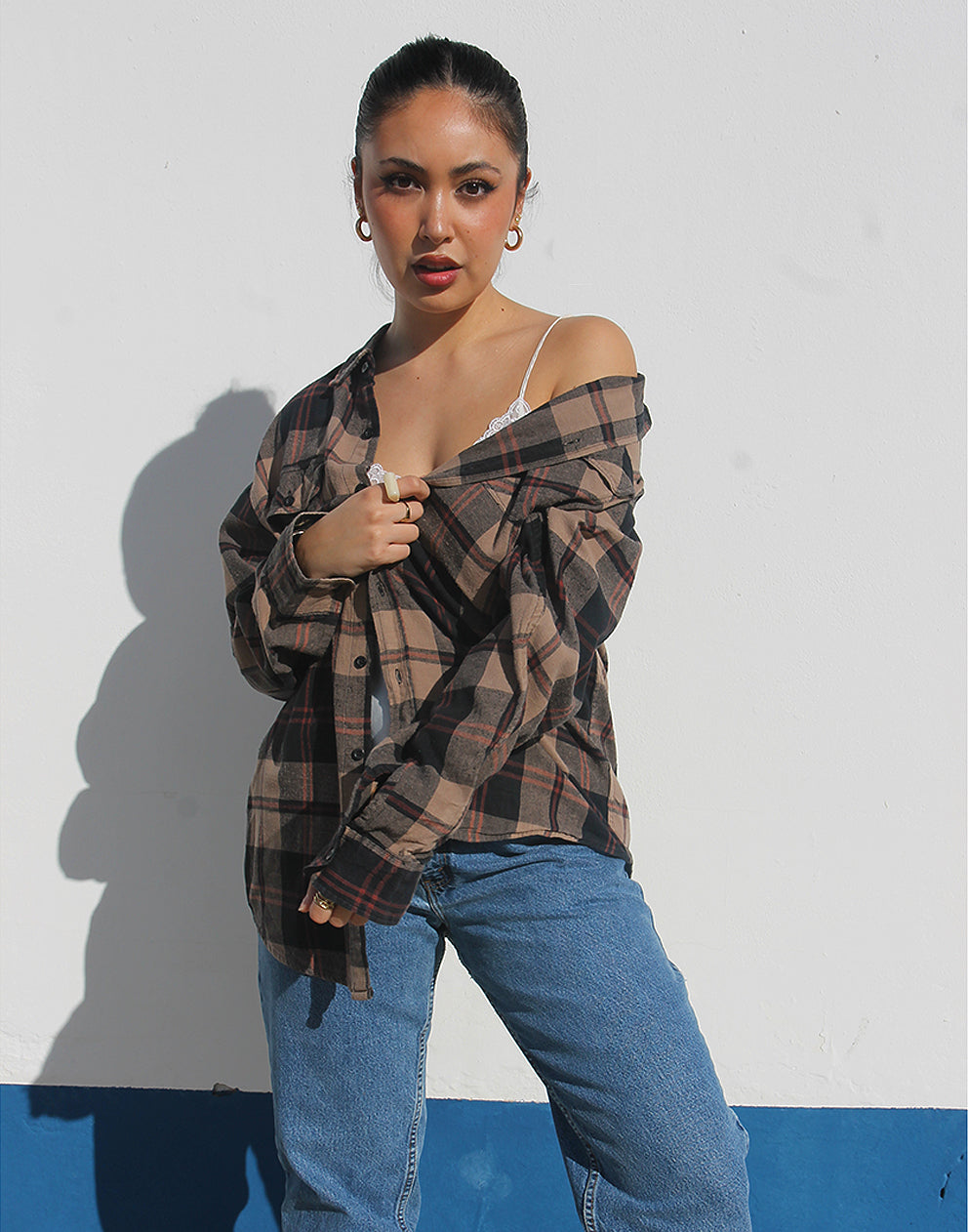 Woman wearing a brown plaid shirt and womens vintage jeans against a white background