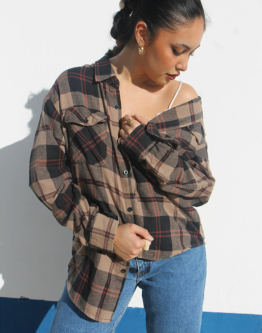 Woman wearing a brown plaid shirt and jeans against a white background