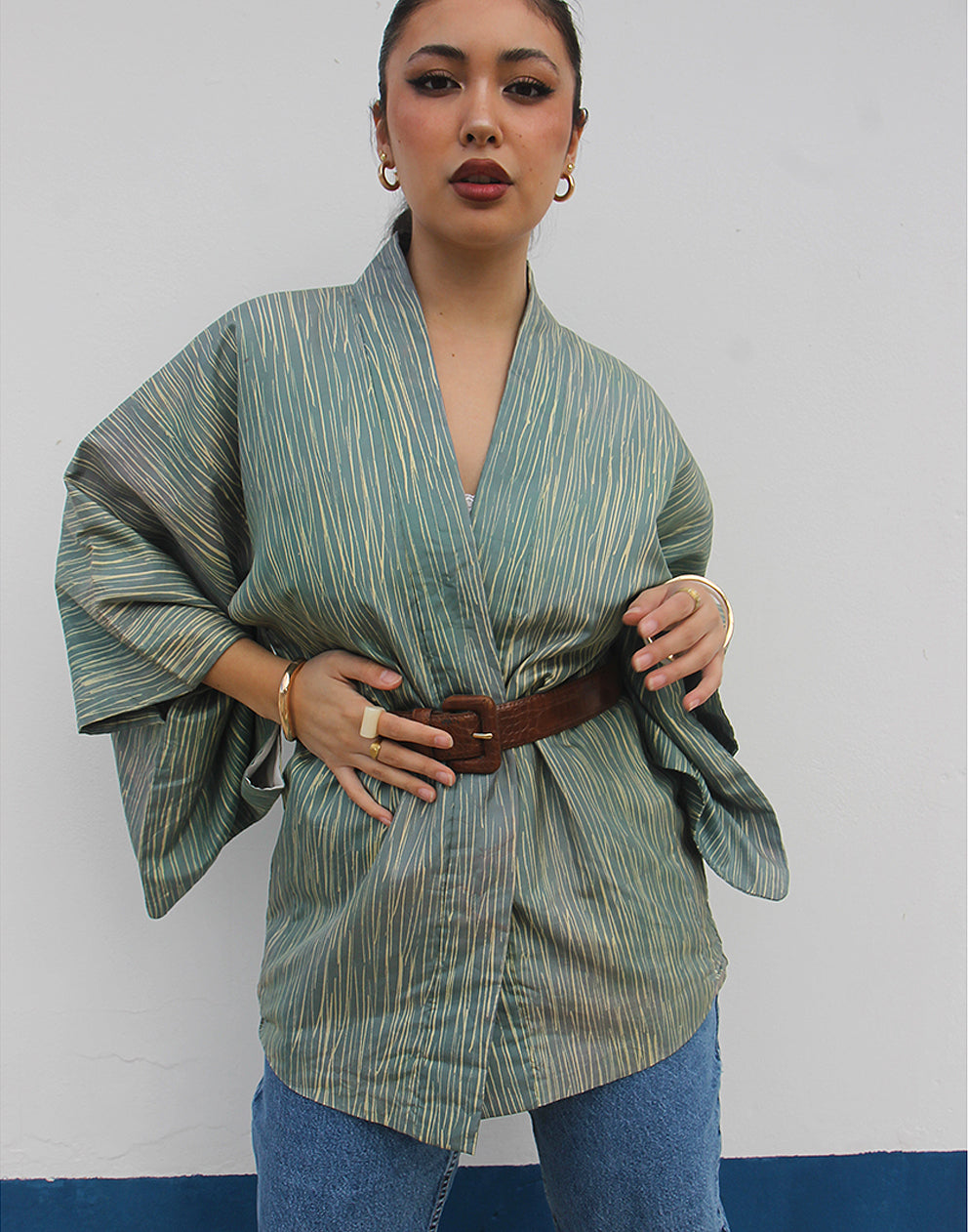 WOMAN WEARING GREEN HAORI KIMONO JACKET AGAINST A WHITE WALL