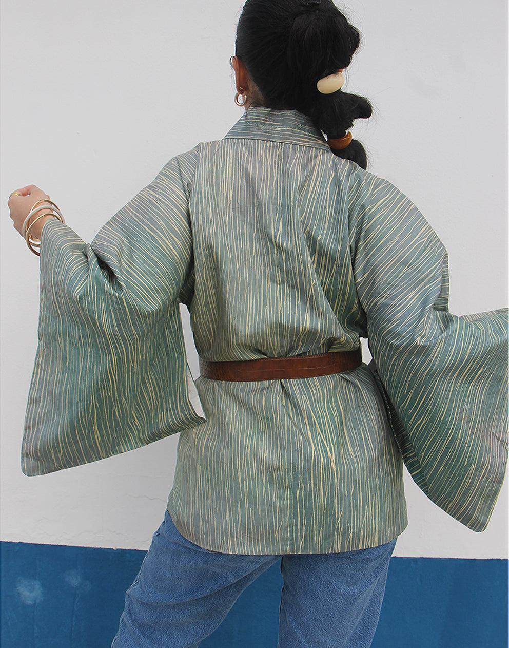 WOMAN WEARING GREEN HAORI KIMONO JACKET AGAINST A WHITE WALL