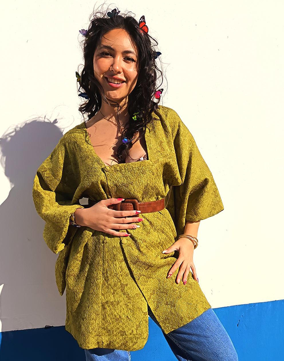 Person wearing a green textured Michiyuki kimono with a belt, standing against a blue and white background.