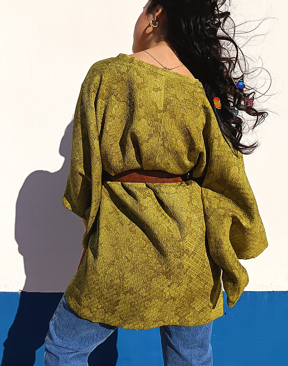 Person wearing a green textured Michiyuki kimono with a belt, standing against a blue and white background.