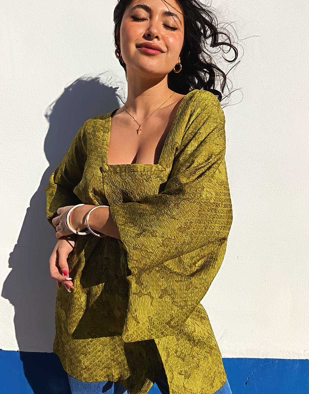 Person wearing a green textured Michiyuki kimono with a belt, standing against a blue and white background.