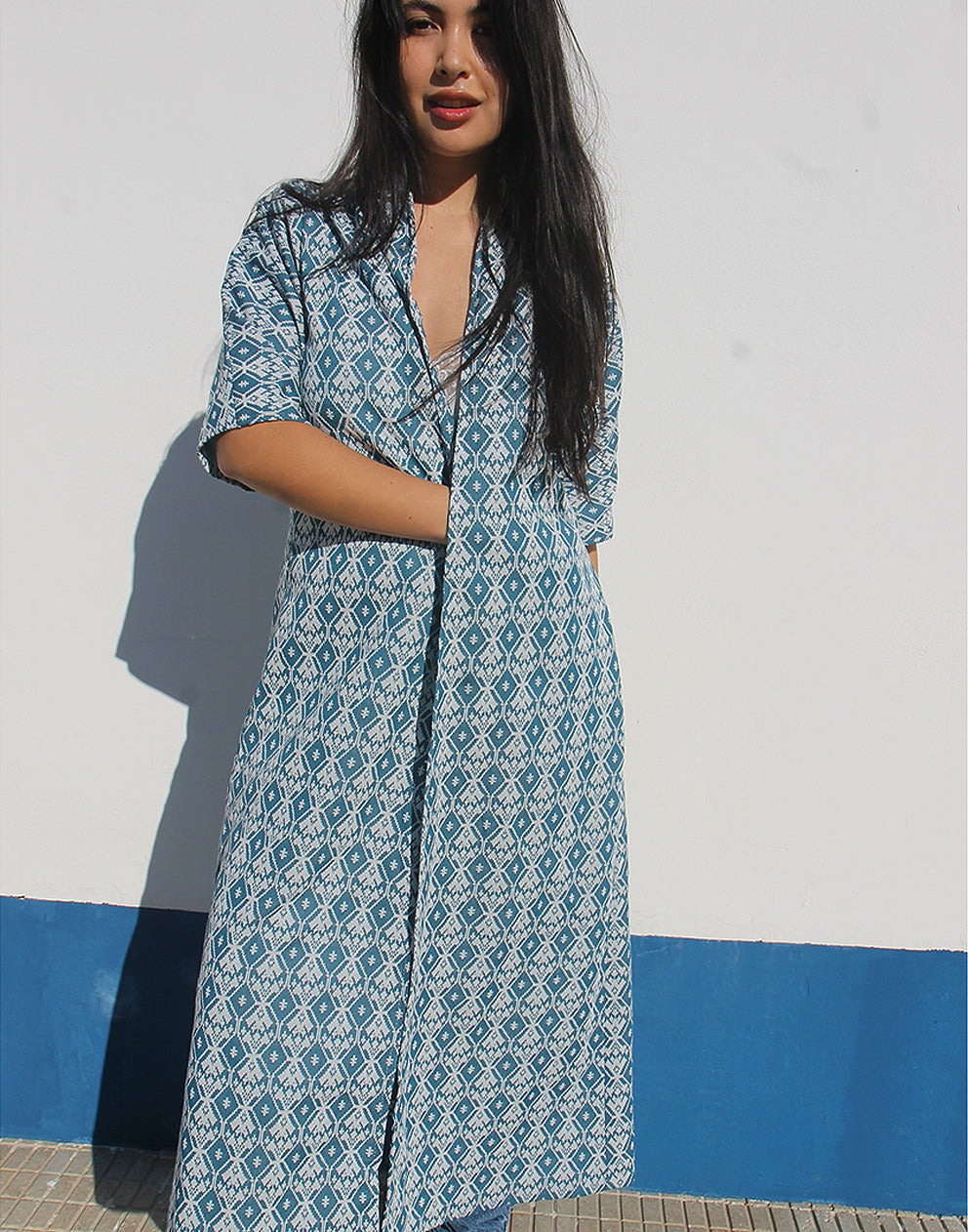 WOMAN WEARING A LONG BLUE JACKET AGAINST A WHITE WALL 