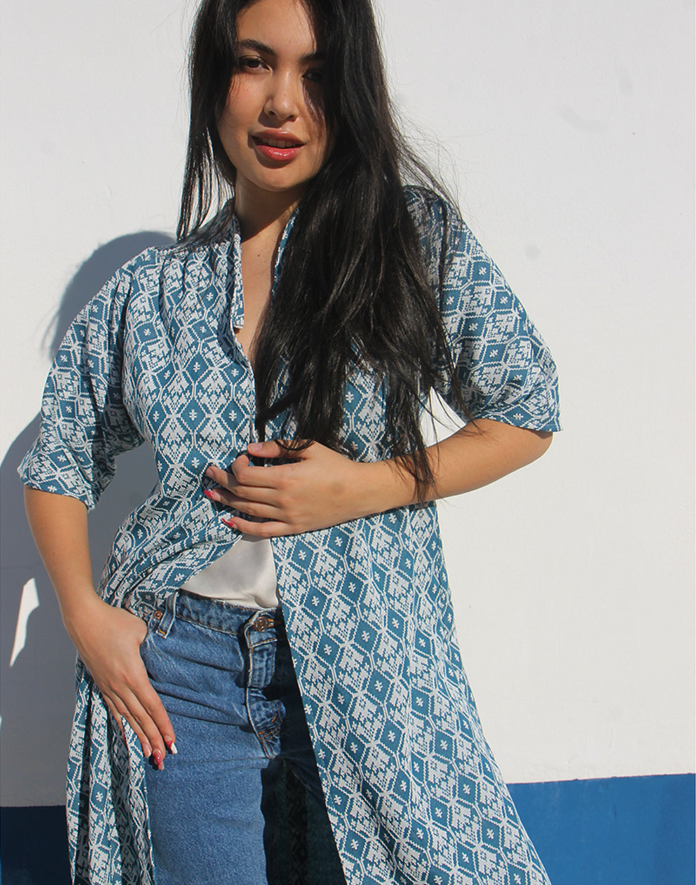 WOMAN WEARING A LONG BLUE JACKET AGAINST A WHITE WALL 
