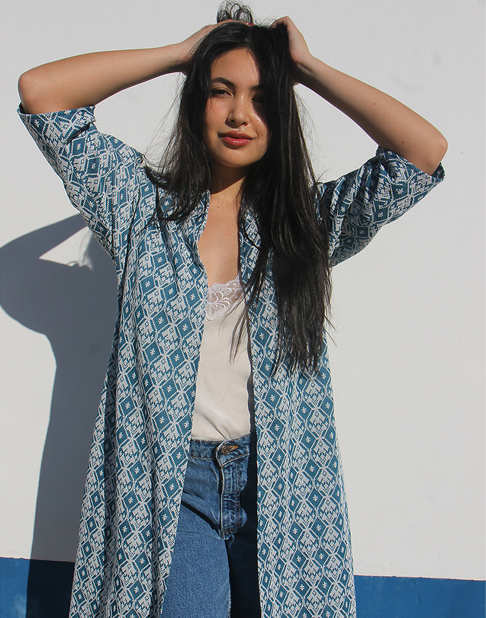 WOMAN WEARING A LONG BLUE JACKET AGAINST A WHITE WALL 