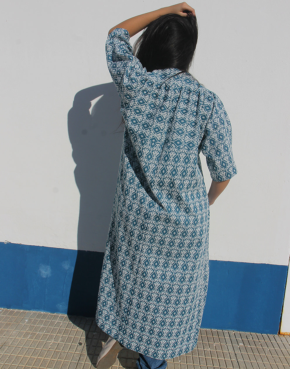 WOMAN WEARING A LONG BLUE JACKET AGAINST A WHITE WALL 