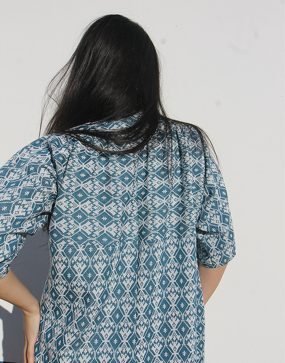 WOMAN WEARING A LONG BLUE JACKET AGAINST A WHITE WALL 