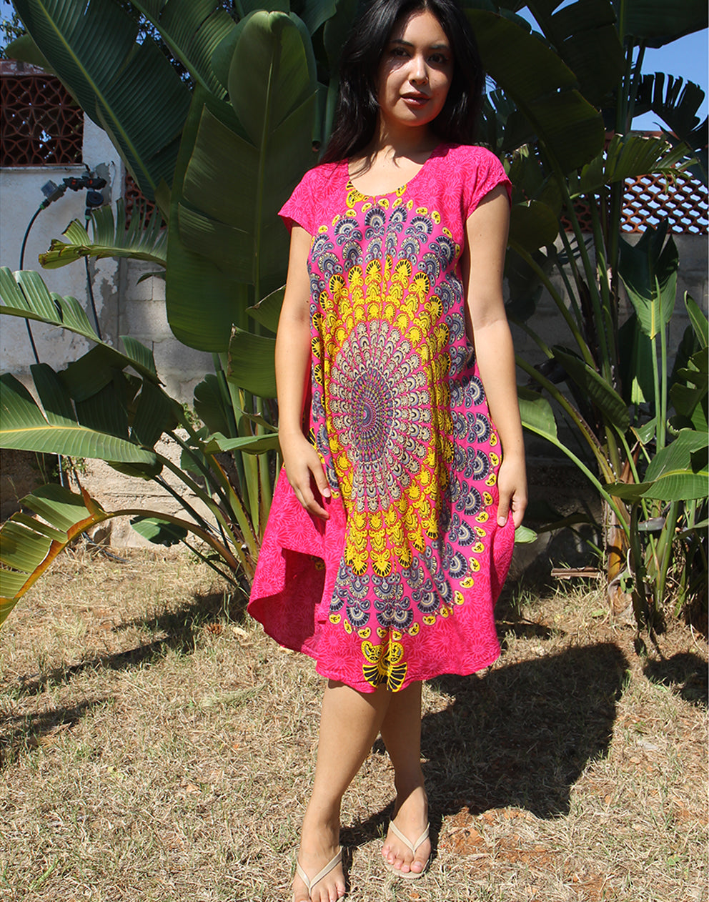 A woman wearing a bright pink beach dress with a large yellow print, standing outdoors