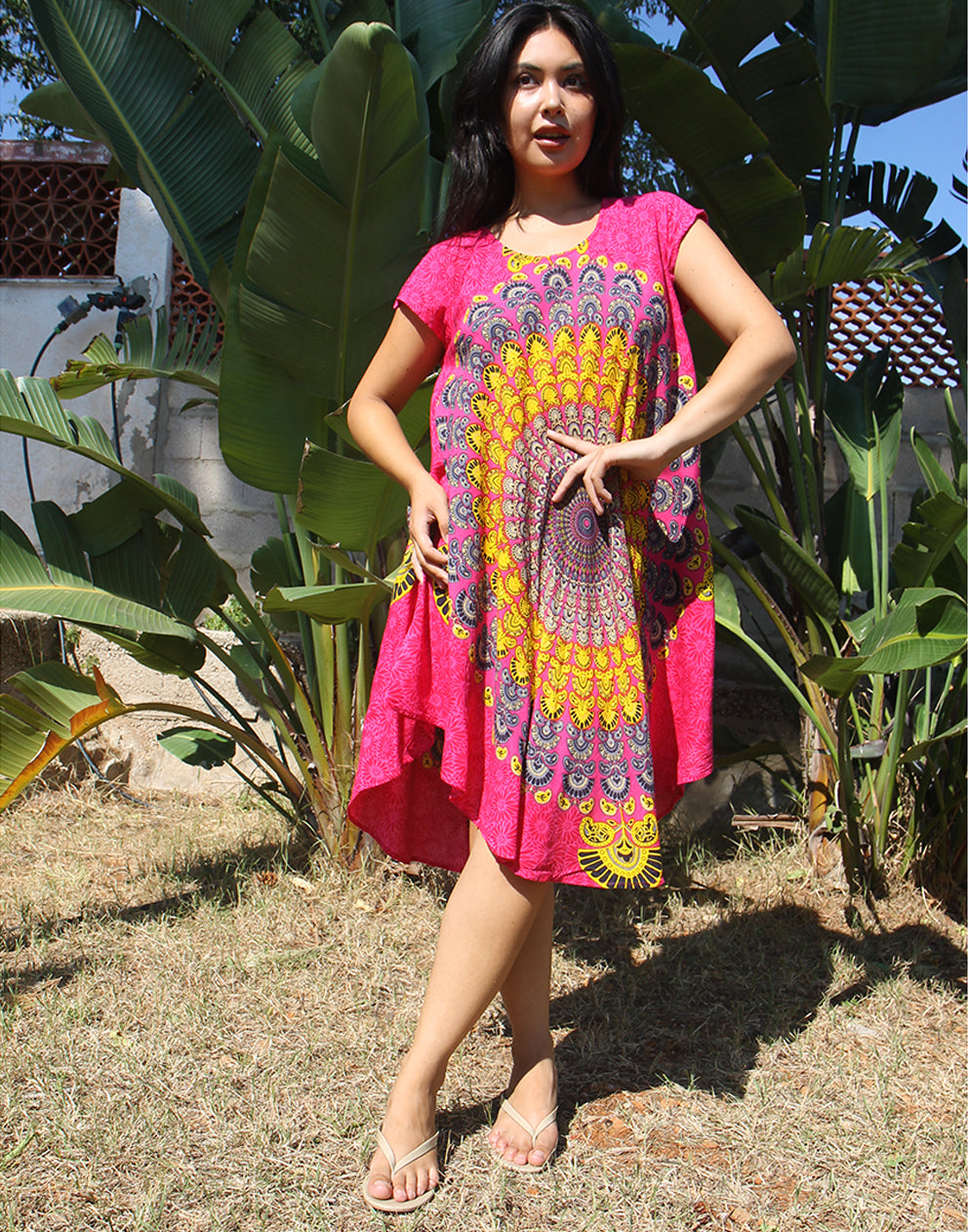A woman wearing a bright pink beach dress with a large yellow print, standing outdoors