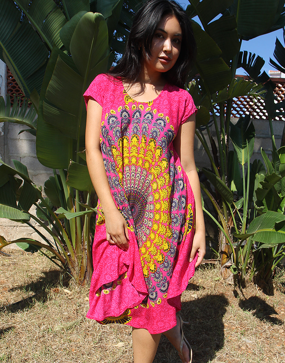 A woman wearing a bright pink beach dress with a large yellow print, standing outdoors