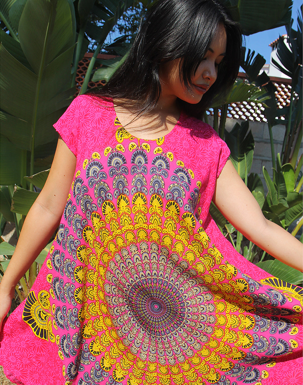 A woman wearing a bright pink beach dress with a large yellow print, standing outdoors