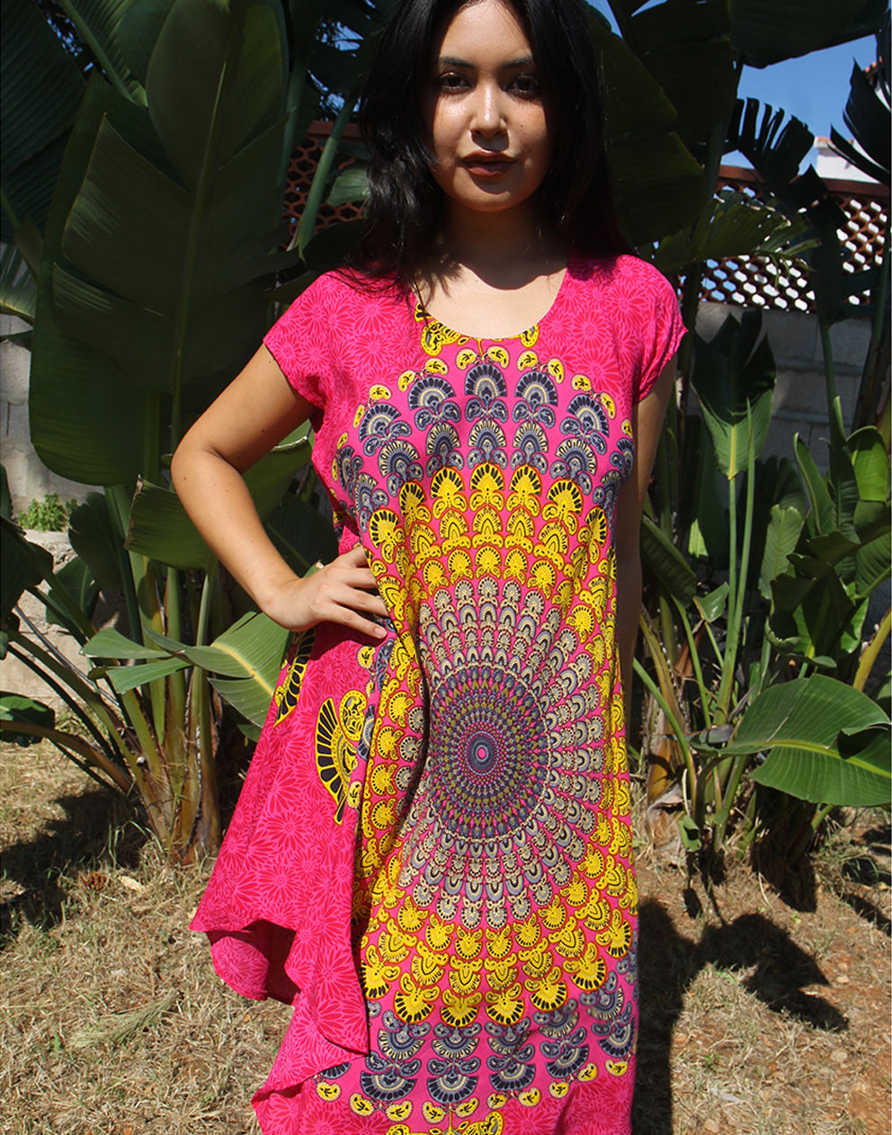 A woman wearing a bright pink beach dress with a large yellow print, standing outdoors