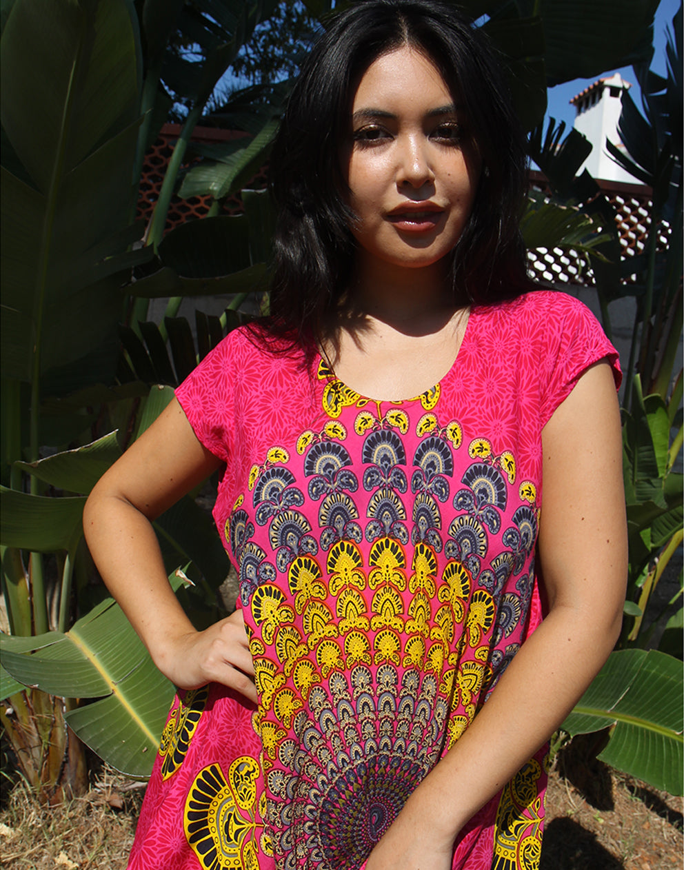 A woman wearing a bright pink beach dress with a large yellow print, standing outdoors