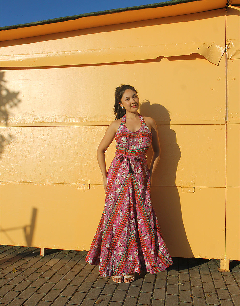 woman wearing 70s pink sleeveless maxi dress against a yellow wall